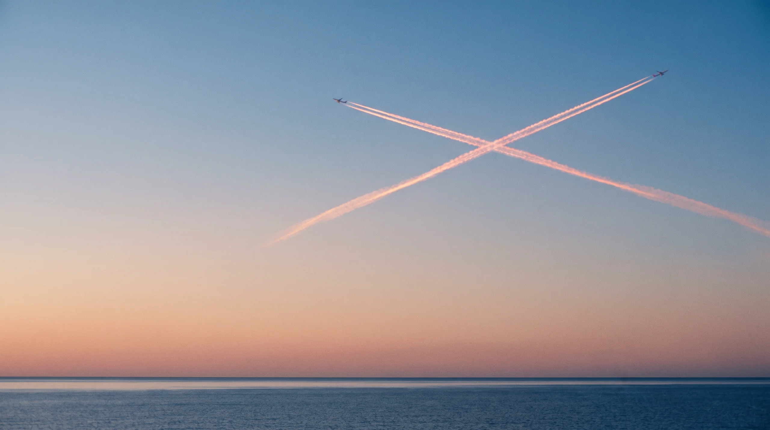 Two aircraft contrails crossing in the sky at twilight.
